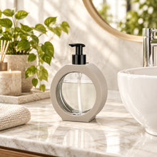 Load image into Gallery viewer, Beige ring-frame glass soap dispenser beside a basin
