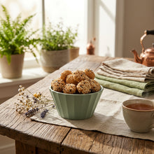 Load image into Gallery viewer, Green bowl filled with sesame seed balls on a wooden table.
