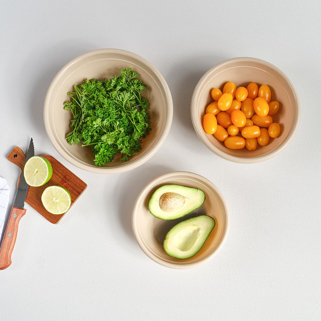 Three bowls with fresh ingredients including parsley, cherry tomatoes, and avocado halves on a light gray background.