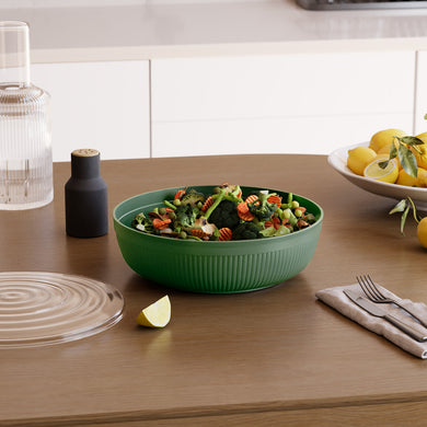 Green salad bowl with a salad on a wooden table with lemons and a glass bottle in the background.