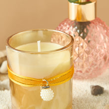 Load image into Gallery viewer, Decorative candle in a glass holder with a yellow ribbon and pearl charm, set against a neutral background.
