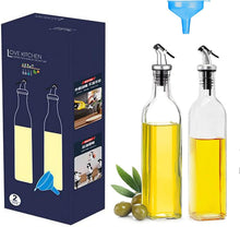 Load image into Gallery viewer, A 2-piece glass oil dispenser set with metal pour spouts, shown with its dark blue retail box, olive branches, olives, and a blue funnel on a white background.
