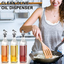 Load image into Gallery viewer, Three clear glass oil bottles with black pour spouts filled with orange, yellow, and red oils, shown next to a woman in a kitchen using a wooden spatula in a pan. Text at the top reads 'CLEAN OLIVE OIL DISPENSER'.
