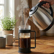 تحميل الصورة في عارض المعرض، Person pouring hot liquid from a kettle into a French press on a wooden table.
