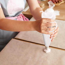Load image into Gallery viewer, Person decorating with a cream pastry bag, preparing cupcake frosting on parchment paper.
