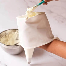 Load image into Gallery viewer, Hand holding a cream-filled pastry bag for cupcake decoration, with a mixing bowl in the background.
