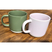 Load image into Gallery viewer, Two mugs, one green and one white, on a wooden surface.

