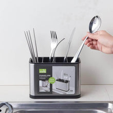 تحميل الصورة في عارض المعرض، Silverware holder with cutlery and a hand picking up a spoon, on a light background.
