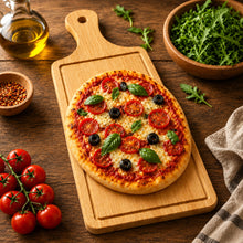 تحميل الصورة في عارض المعرض، A small round pizza topped with tomato slices, black olives, and fresh basil leaves, served on a wooden cutting board on a rustic wooden table. Surrounding props include a bottle of olive oil, a bowl of arugula, a small bowl of red pepper flakes, cherry tomatoes on the vine, and a cloth napkin.
