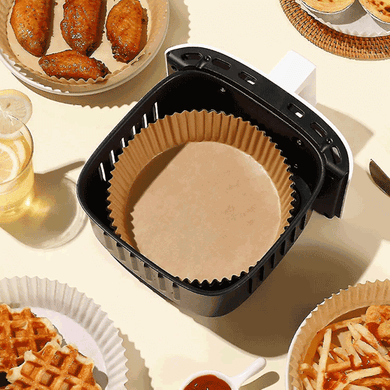 Non-stick disposable air fryer paper liner in black air fryer basket surrounded by cooked food.