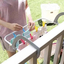 Load image into Gallery viewer, Person using a clothespin holder with colorful clothespins on a railing.
