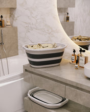 تحميل الصورة في عارض المعرض، Black and white striped folding bathtub on a bathroom counter with toiletries.

