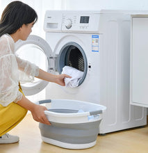 تحميل الصورة في عارض المعرض، Woman using a washing machine with a collapsible laundry basket on a wooden floor.
