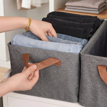 Load image into Gallery viewer, Person organizing folded clothes into a gray storage bin with brown handles.
