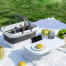 Load image into Gallery viewer, Outdoor picnic setup with a cooler, table, and food items on a blanket.
