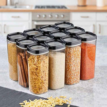 تحميل الصورة في عارض المعرض، A set of clear plastic canisters with black lids, filled with various dry goods like pasta, cinnamon sticks, rice, beans, and lentils, arranged on a kitchen countertop.
