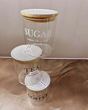 Load image into Gallery viewer, Two glass jars with decorative lids on a beige surface
