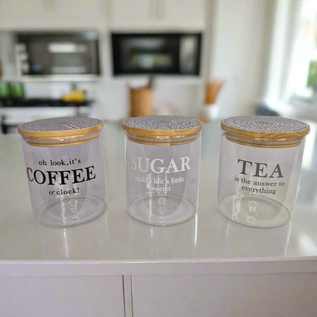 Three glass jars with wooden lids labeled 'Coffee', 'Sugar', and 'Tea' on a kitchen counter.