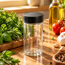 تحميل الصورة في عارض المعرض، A small clear glass jar with a black screw-on lid, placed on a wooden tabletop.
