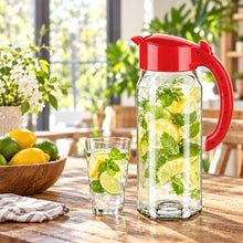 تحميل الصورة في عارض المعرض، Red pitcher with water and lemon slices on a wooden table with a blurred kitchen background
