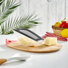 Load image into Gallery viewer, A stainless steel grater with a detachable container is used to grate cheese on a wooden cutting board, with a lemon, tomato, and other kitchen items in the background.
