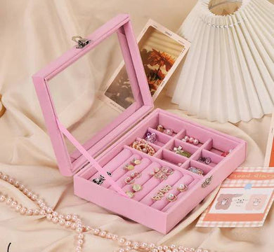Pink jewelry box with compartments filled with jewelry on a beige surface.