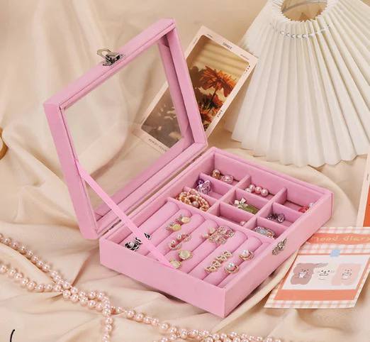 Pink jewelry box with compartments filled with jewelry on a beige surface.