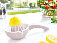 Load image into Gallery viewer, Handheld lemon squeezer on a white surface with lemons and a salad in the background.
