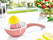 Load image into Gallery viewer, Pink manual juicer with a lemon on a white surface, with a blurred background of vegetables.
