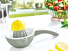 Load image into Gallery viewer, Gray manual lemon squeezer with a lemon on a white surface, with a blurred background of a kitchen.
