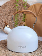 Load image into Gallery viewer, White kettle with wooden handle and base on a woven mat, featuring the Vicalina brand.
