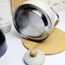 Load image into Gallery viewer, White ceramic pot with metal lid on a wooden trivet, surrounded by kitchen items.
