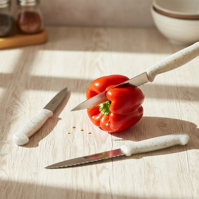 Red bell pepper being sliced with a knife on a wooden surface