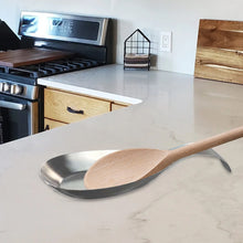 تحميل الصورة في عارض المعرض، Wooden spoon on a metal trivet on a kitchen counter with an oven in the background.
