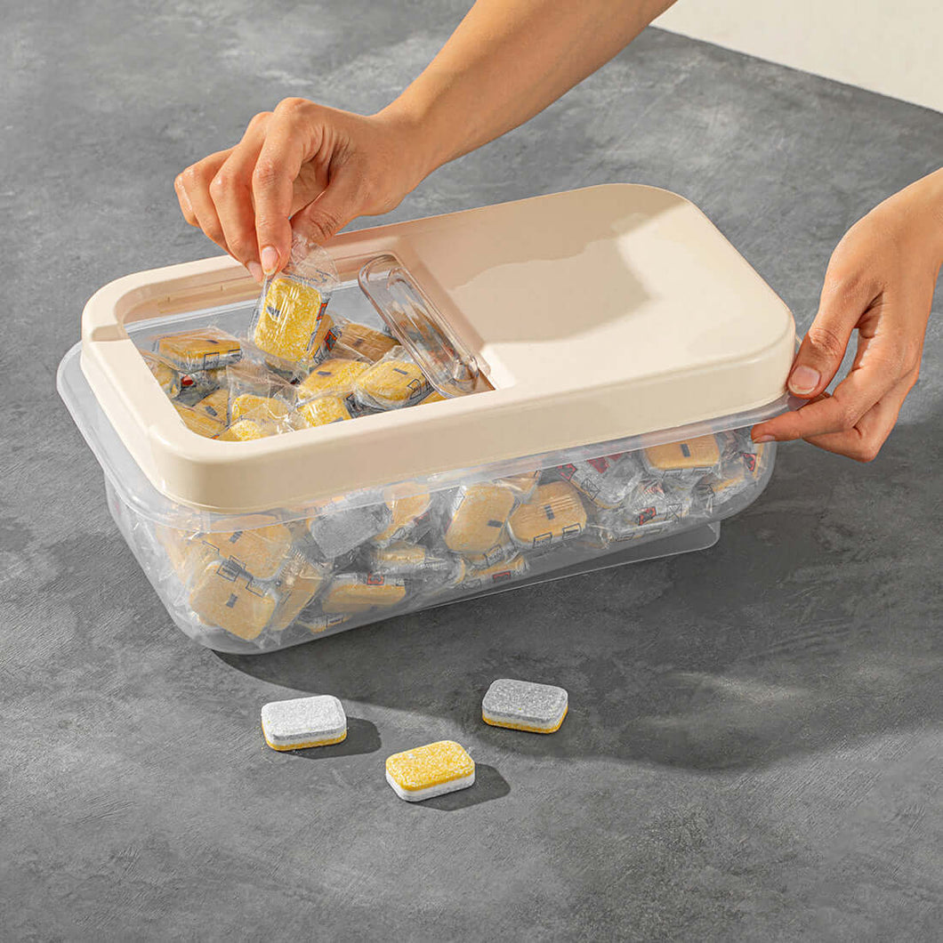 A large clear plastic storage container with a slide lid, being held by a person. The container is filled with small, sealed packages of rice, and there are a few additional packages visible outside the container.