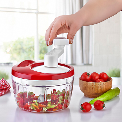 Hand using a red and white manual food chopper with vegetables on a table.