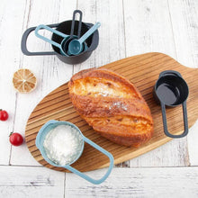 تحميل الصورة في عارض المعرض، Loaf of bread on a wooden board with measuring cups and a salt shaker on a white surface.
