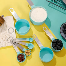 Load image into Gallery viewer, Set of turquoise measuring cups with various measurements filled with different ingredients on a yellow and blue background.
