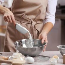 تحميل الصورة في عارض المعرض، Person in a kitchen pouring flour into a metal bowl with various baking ingredients on the counter.

