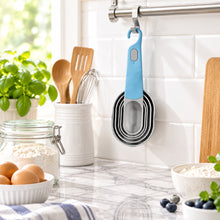تحميل الصورة في عارض المعرض، Set of measuring cups with blue handles hanging on a rack with a yellow mat in the background.
