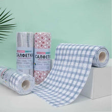 Load image into Gallery viewer, Blue and white checkered cotton napkins, with one unrolled on a white block and two rolls standing behind it, set against a mint green background with a small palm leaf in the corner.
