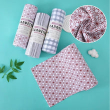 Load image into Gallery viewer, Three rolled fabric cloths with labels are arranged on a turquoise background beside an unfolded matching cloth and a circular inset showing the fabric pattern. The cloths appear in gingham and floral prints, with small green leaves and white cloud-like props around them.
