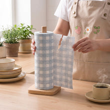 Load image into Gallery viewer, Person holding a roll of plaid paper towel with a cylindrical roll on a wooden surface.
