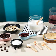 Load image into Gallery viewer, A styled tabletop arrangement of small ceramic bowls, wooden spoons, a glass jar of white sugar with a wooden scoop, coffee beans, red berries, and a glass of red wine against a teal background.
