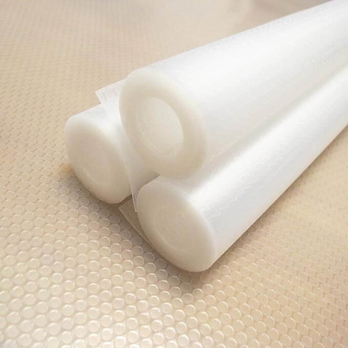 Two rolls of white non-slip shelf liner placed on a textured surface.