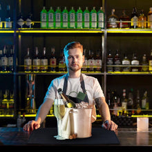Load image into Gallery viewer, Barista with a bag of coffee and a bottle of wine in a bar setting
