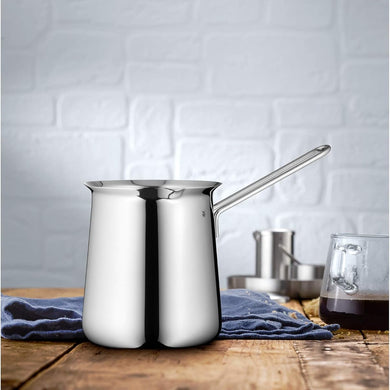 Stainless steel milk frothing pitcher on a wooden surface with a white brick wall background