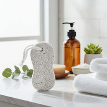 Load image into Gallery viewer, White pumice stone on a marble surface with towels and a bottle in the background
