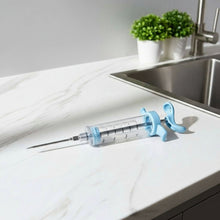 Load image into Gallery viewer, Syringe with blue plunger on a white surface near a sink

