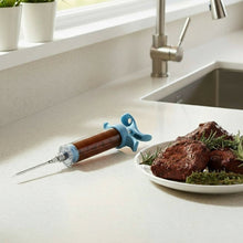 Load image into Gallery viewer, Marinade injector on a kitchen counter with a plate of meat and herbs.
